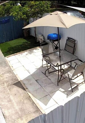Eine Terrasse mit einem Metalltisch und Stühlen, einem Grill und einem großen Sonnenschirm.