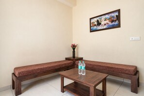 Una habitación con un sofá marrón, una mesa de madera con dos botellas de agua, un jarrón con flores y un cuadro de caballos en la pared.