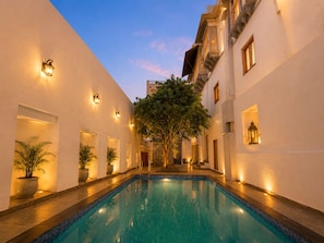 A pool area with a clear blue pool, white walls, and warm lighting. - Hari Priya Resort Udaipur (Udaipur)