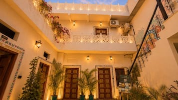 Un patio con un espacio abierto en el centro, plantas en macetas, una escalera y un balcón con barandillas decorativas.