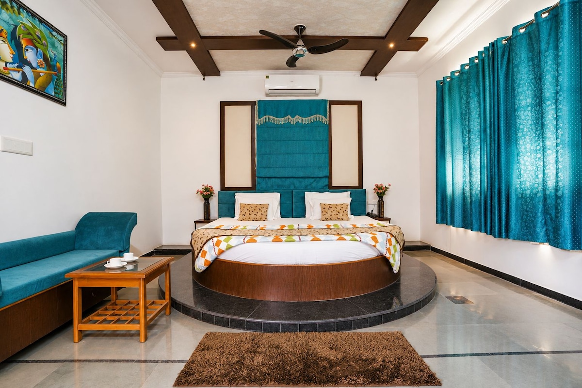 Una habitación de hotel con una cama redonda, un sofá, una mesita y un ventilador de techo.