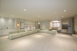 Una sala moderna con un amplio sofá modular en forma de L, una cocina integrada y una zona de estar con una mesa pequeña y sillas.
