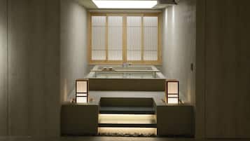 Un baño minimalista con lavamanos empotrado, una ventana con persianas verticales y un pequeño escalón que lleva a una zona con guijarros.