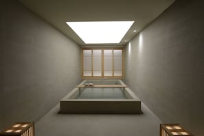 A modern bathroom with a skylight, a bathtub, and a window with wooden blinds. - VODASTAY 2-3 (Busan)