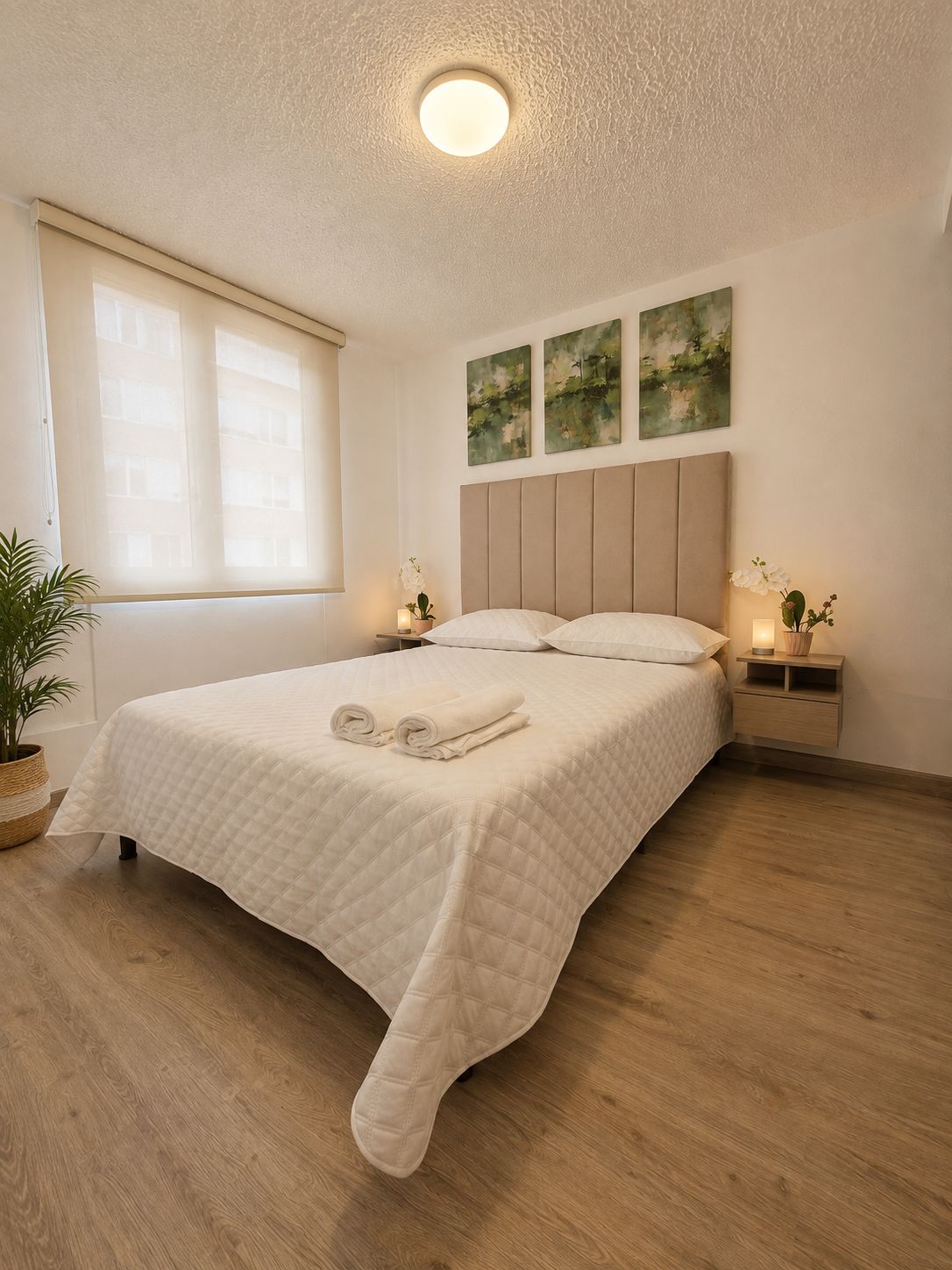 A bedroom with a bed, bedside tables, a potted plant, and artwork on the wall.