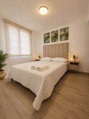 A bedroom with a bed, bedside tables, a potted plant, and artwork on the wall. - DORÉ 26 | Modern accommodations near El Dorado (Bogotá)