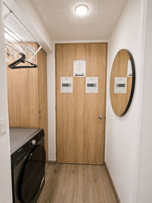 A laundry room with a washing machine, a drying rack, and a wooden door with welcome and informational cards. - DORÉ 26 | Modern accommodations near El Dorado (Bogotá)