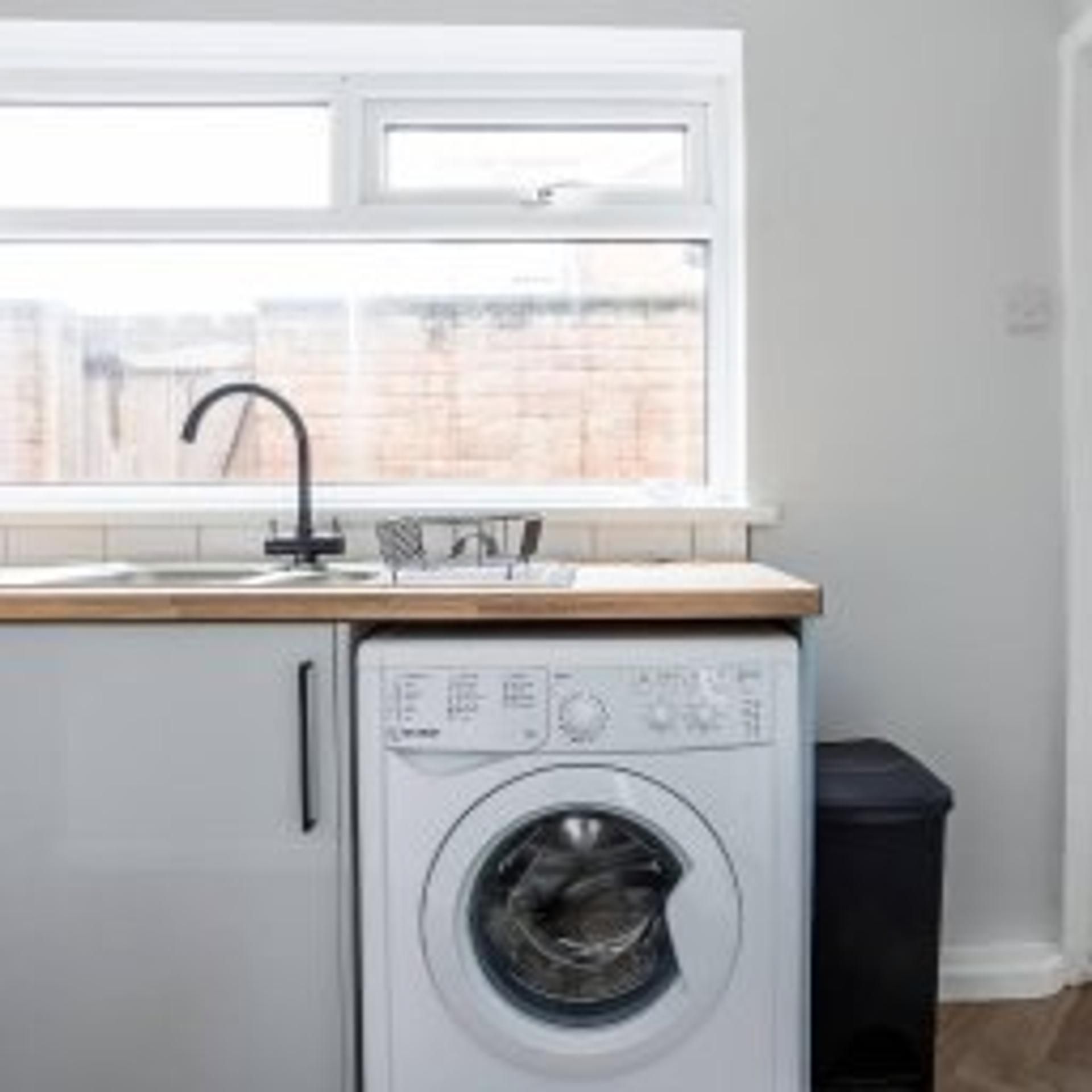 A compact laundry area with a washing machine, a sink, and a window.