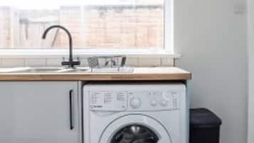 A compact laundry area with a washing machine, a sink, and a window.