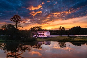 A house with a large deck, surrounded by trees and a body of water reflecting the sky. - Spacious 20-bedroom Waterfront Retreat. Pool, Dock, 15 Boat Slips & Bay VIEWS! (Tilghman Island)