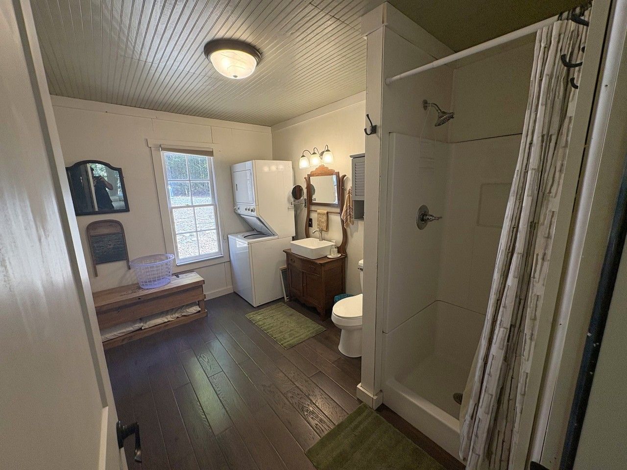 A compact bathroom with a shower, toilet, sink, and a small window.