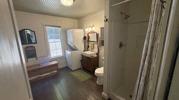 A compact bathroom with a shower, toilet, sink, and a small window.