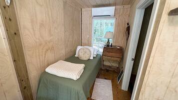 Une petite chambre à coucher, chaleureuse et accueillante, avec un lit simple, une table de chevet, une lampe et une fenêtre laissant entrer la lumière naturelle.