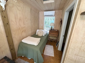 A small, cozy bedroom with a single bed, a nightstand, a lamp, and a window providing natural light. - Farmhouse and Bunkhouse on 14 Wooded Acres with a Private Pond and Dock (Ronda)