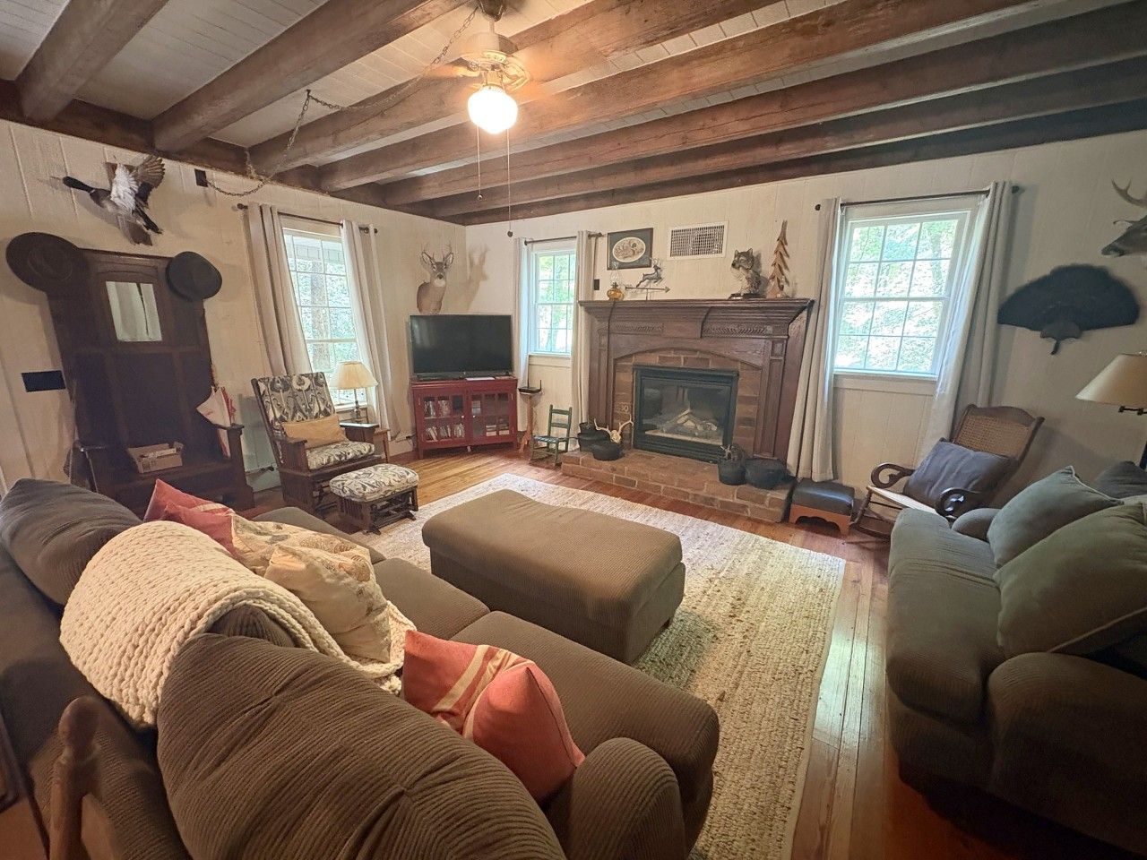 A cozy living room with a fireplace, wooden beams, and a television.