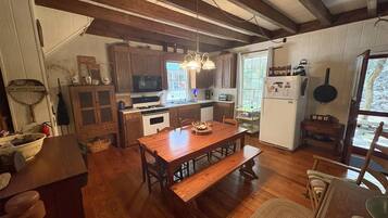 Ein Holztisch mit Bänken, eine Küchenzeile mit Holdekor, ein Kühlschrank und eine Pendelleuchte.