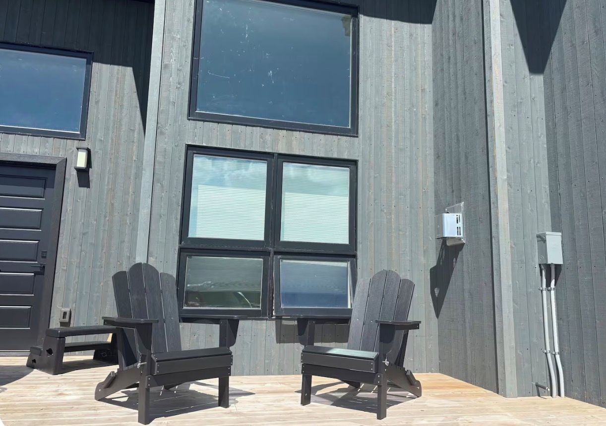 En moderne bygning med store vinduer og en træterrasse med to Adirondack-stole.