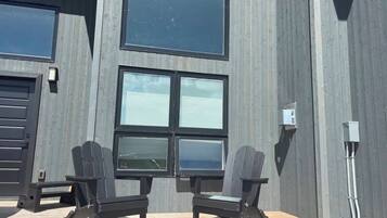 En moderne bygning med store vinduer og en træterrasse med to Adirondack-stole.