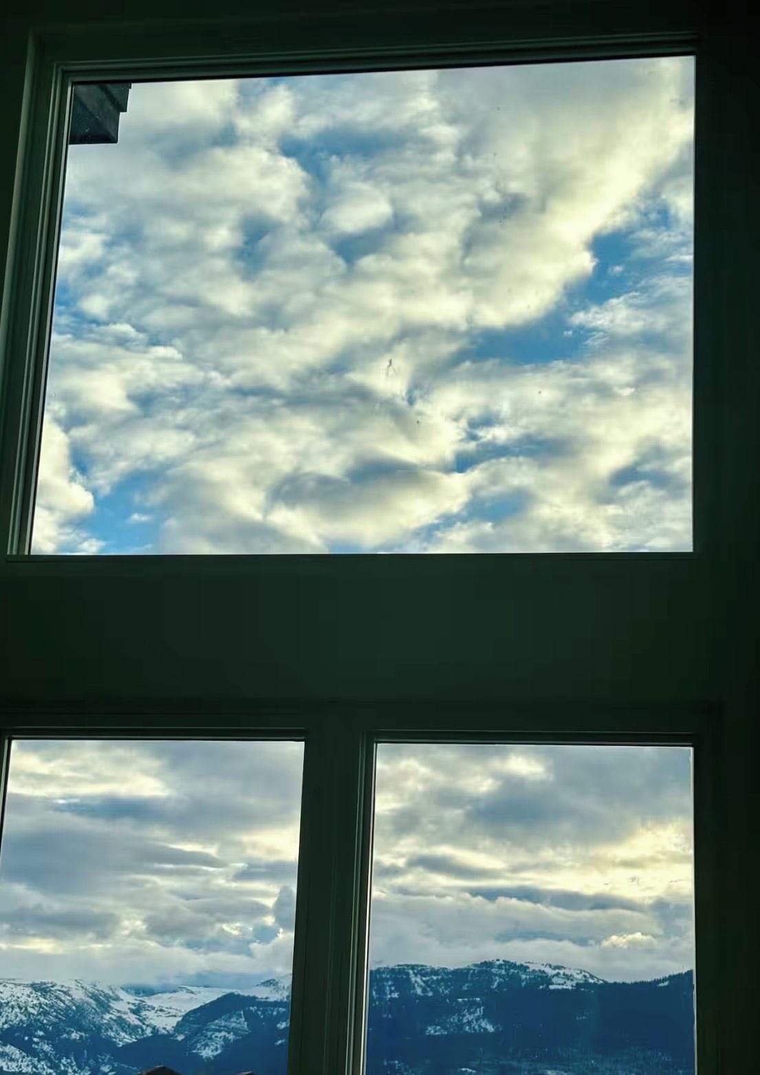 Et vindue med udsigt over et bjerglandskab og en skyet himmel.
