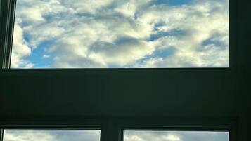 Et vindue med udsigt over et bjerglandskab og en skyet himmel.