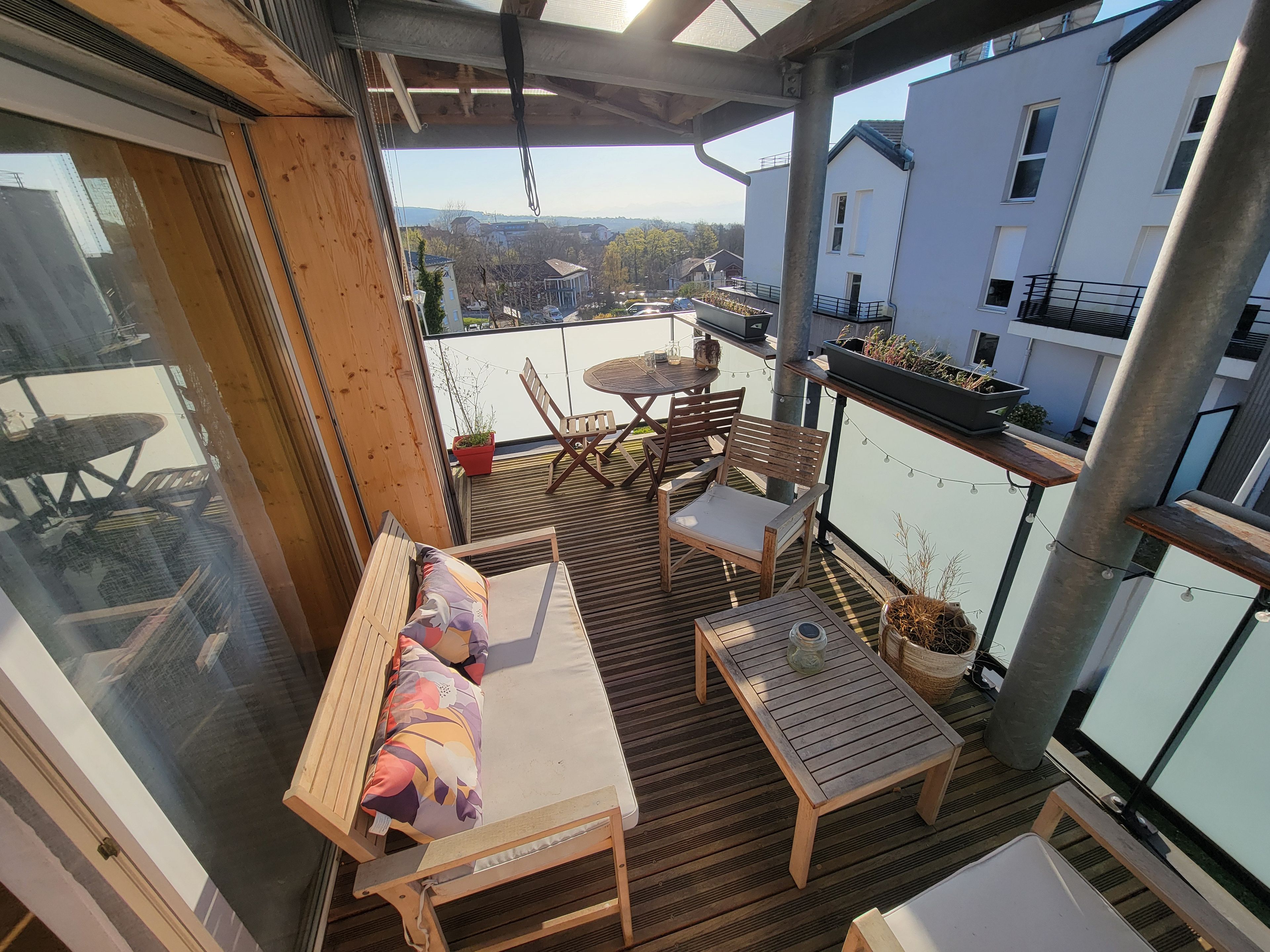 Un balcon agrémenté de meubles en bois, d’une table et de plantes en pot.