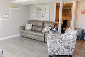 Una sala de estar con un sofá de cuero y un sillón estampado, una mesita auxiliar y un espejo en la pared.