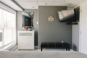 A bedroom with a bed, a dresser, a bench, a mirror, and a television mounted on the wall.