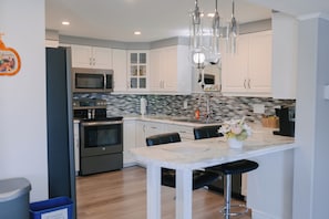 Una cocina moderna con armarios blancos, electrodomésticos de acero inoxidable, encimera de mármol y una zona de bar con taburetes.
