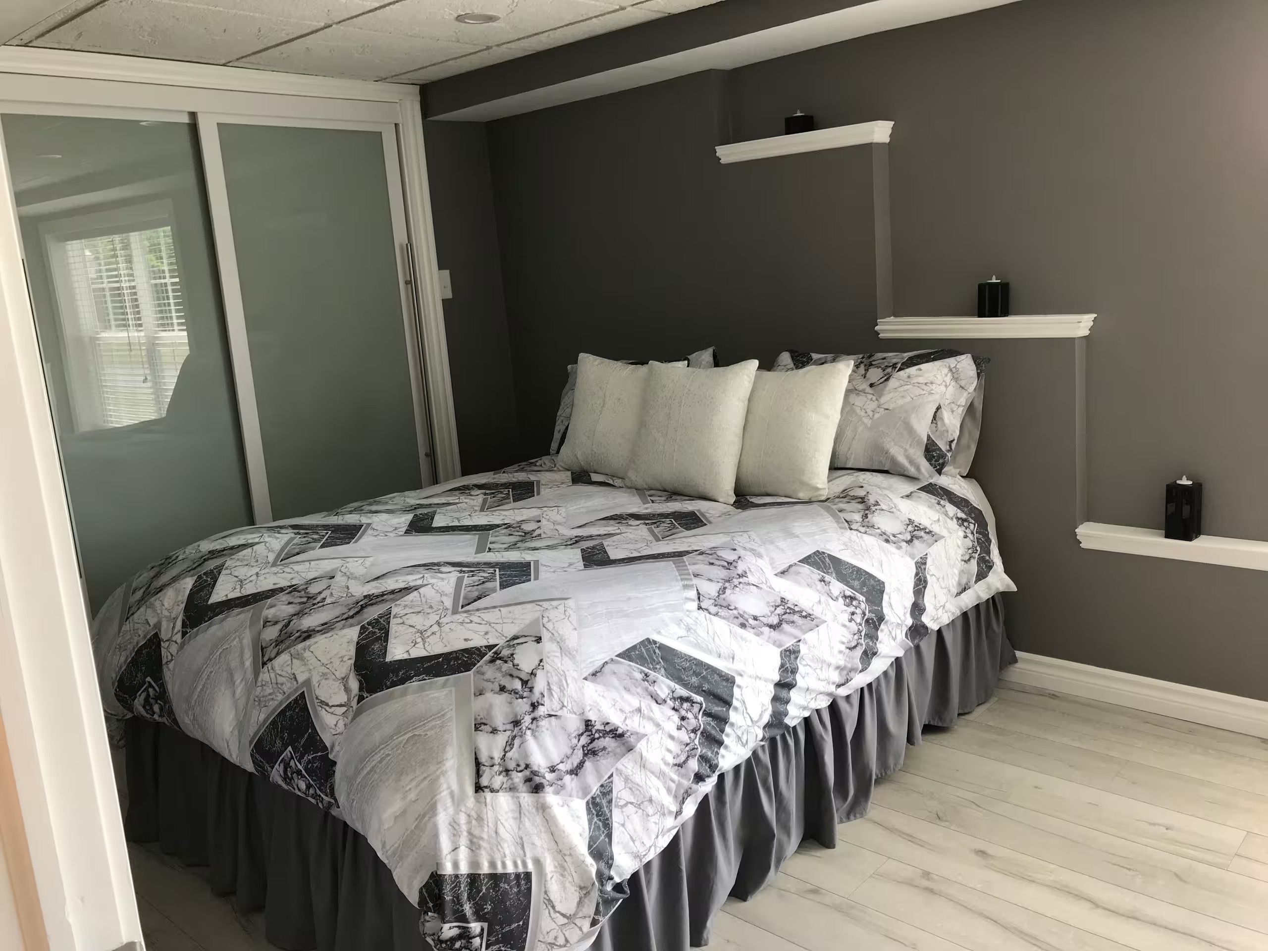 A bedroom with a bed, a sliding door, a dark wall, and a light wooden floor.