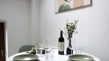 A dining table set with green plates, clear glasses, and cutlery, a bottle of wine, and a vase with flowers.