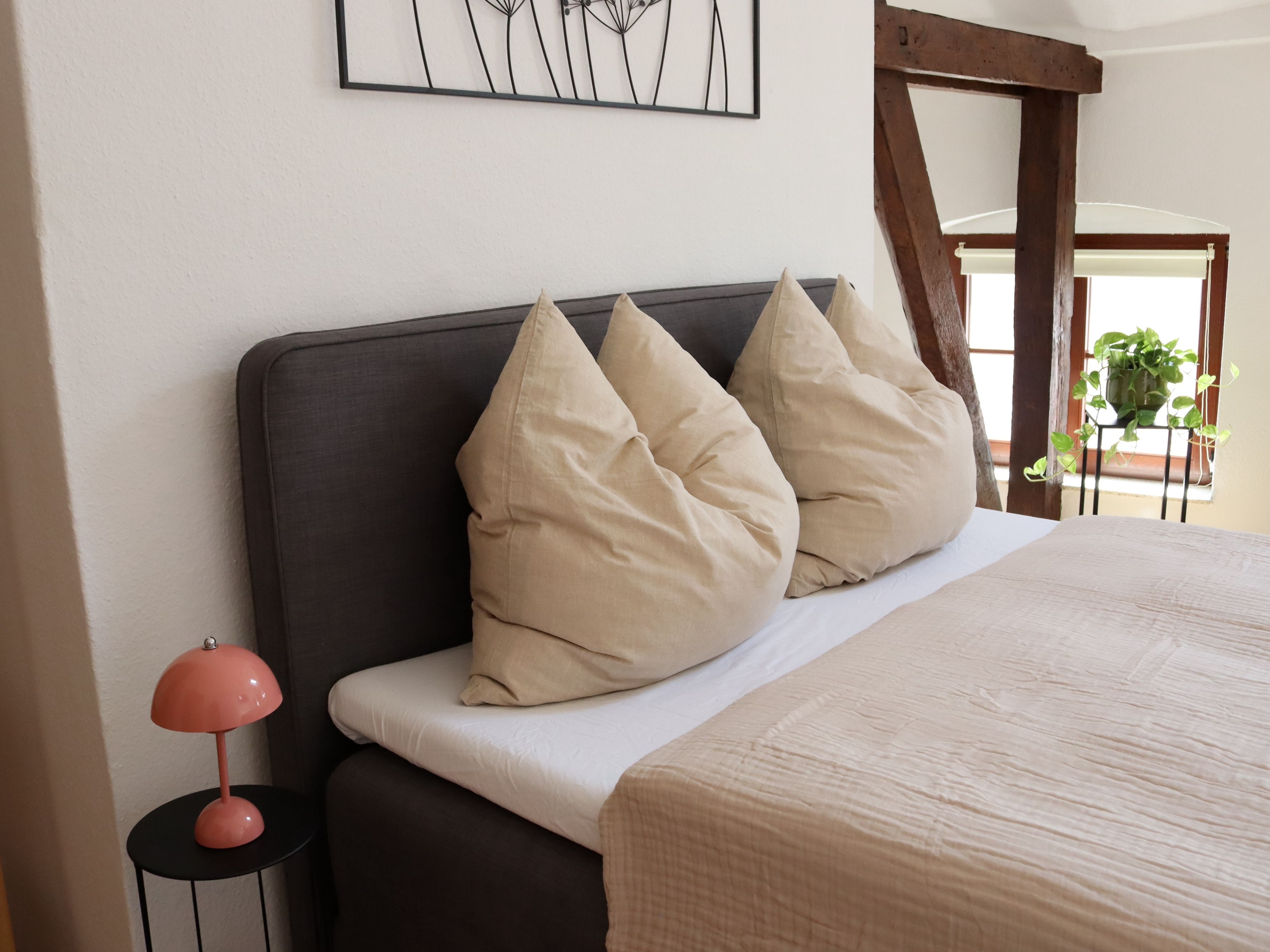 Une chambre à coucher avec un lit, des oreillers, une lampe et une œuvre d’art murale.