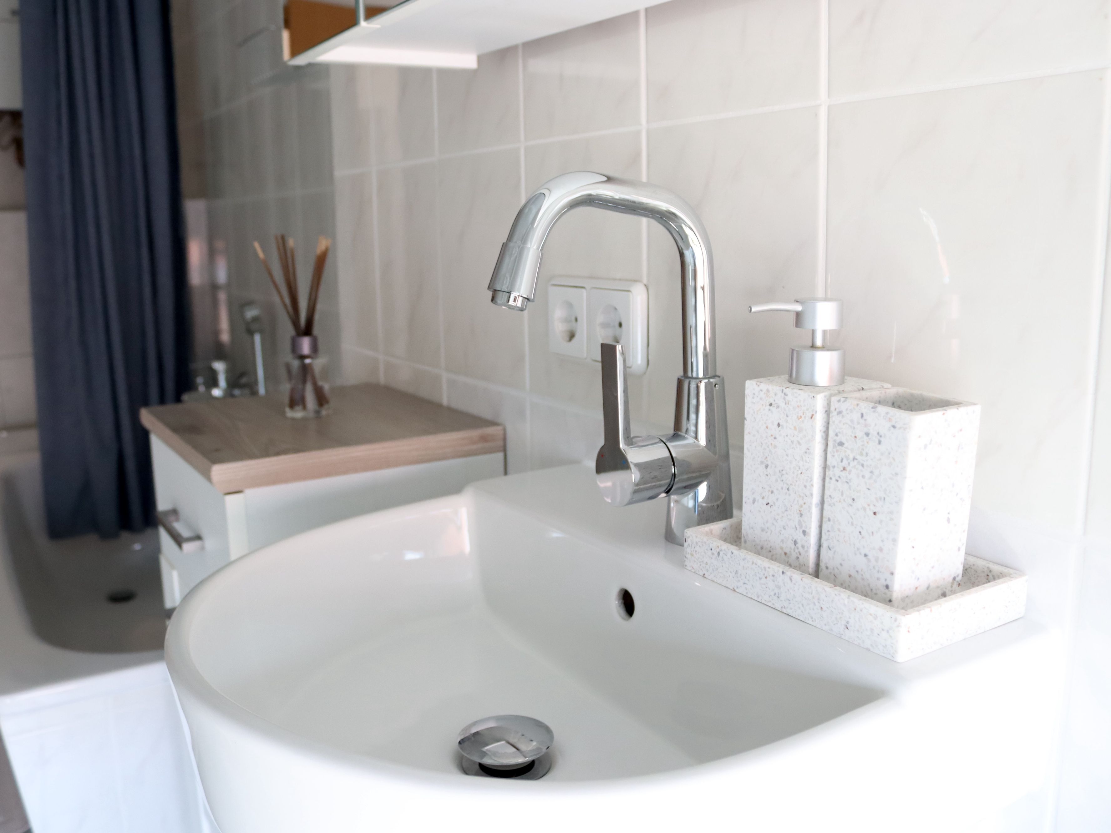 Ein Badezimmer mit einem weißen Waschbecken, einem chromfarbenen Wasserhahn und einer Seifenspender auf einer gefleckten Seifenschale.