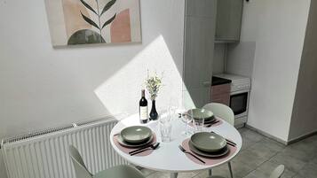 Un comedor con una mesa redonda, sillas, platos, cubiertos y una botella de vino.