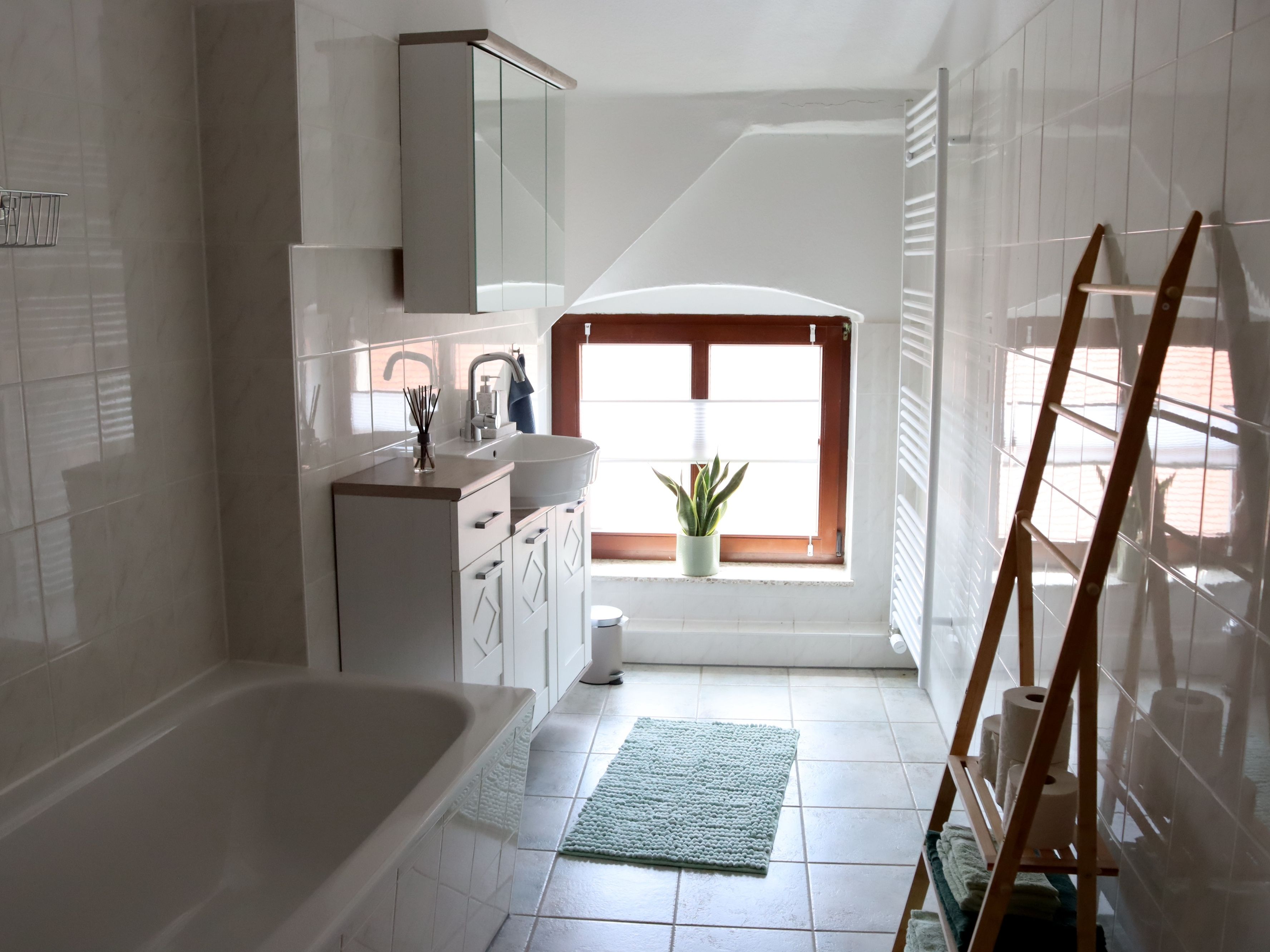 Un baño con bañera, lavamanos, ventana y una planta en maceta.