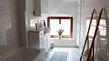 Un baño con bañera, lavamanos, ventana y una planta en maceta.