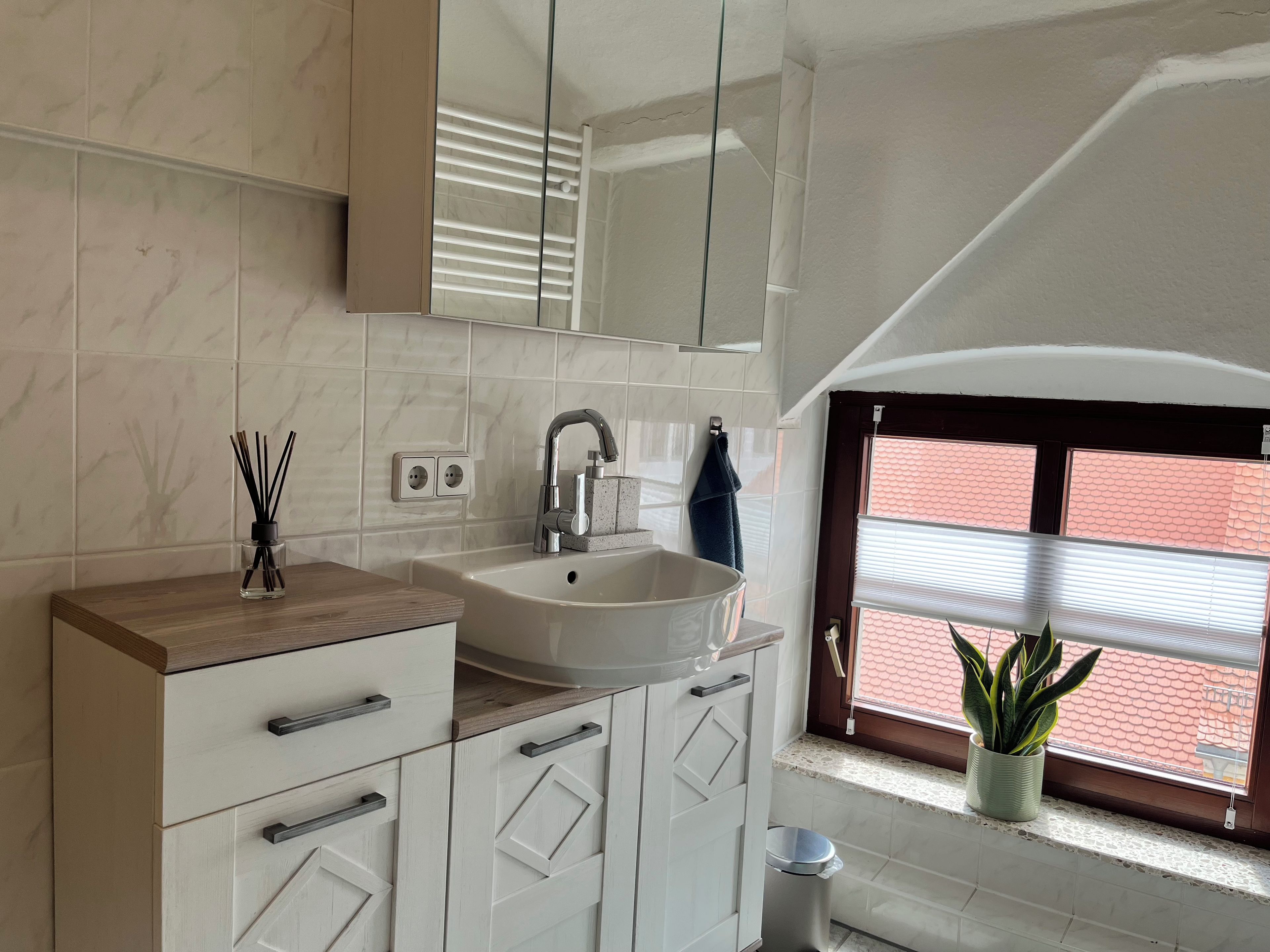 A modern bathroom with a sink, mirror, and window with blinds.