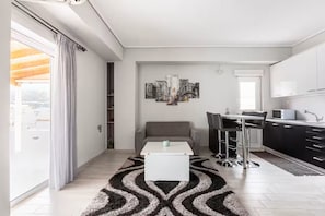 A modern living room with a sofa, a coffee table, and a dining area with a bar stool. There is a kitchen with cabinets and a microwave. - PENTHOUSE IN LOUTRAKI (Loutraki)