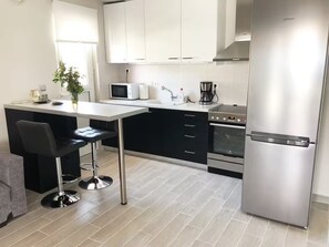 Een moderne keuken met een centraal kookeiland, zwarte barkrukken, een roestvrijstalen koelkast en een inbouwoven.