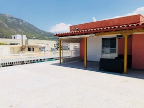 A rooftop terrace with a covered seating area, a closed garage door, and a mountainous backdrop. - PENTHOUSE IN LOUTRAKI (Loutraki)