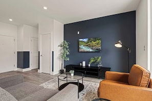 A modern living room with a dark accent wall, a flat-screen TV, a black entertainment unit, a round coffee table, and a leather sofa. - Sleek 1BR | Northern Liberties | Near Fishtown (Philadelphia)