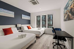 Une chambre d’hôtel avec deux lits, un bureau et une fenêtre donnant sur des immeubles.