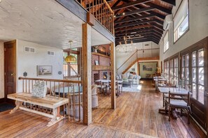 A spacious interior with a wooden staircase, a fireplace, and a dining area with multiple tables and chairs.