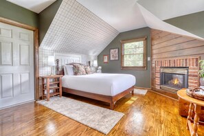 A bedroom with a large bed, a fireplace, a wooden floor, and a sloped ceiling. - Gettysburg Queen Suite for 4 - Fireplace, Sofa Bed, Hot Tub & Sauna (Gettysburg)