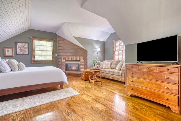 A bedroom with a large bed, a fireplace, a sofa, a television, and wooden flooring. - Gettysburg Queen Suite for 4 - Fireplace, Sofa Bed, Hot Tub & Sauna (Gettysburg)