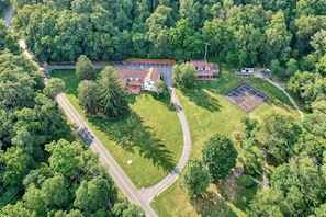 An aerial view of a residential area with a large house, a tennis court, and surrounding greenery.