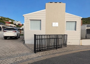 A single-story building with a beige facade, two windows with blinds, and a black metal fence in front.