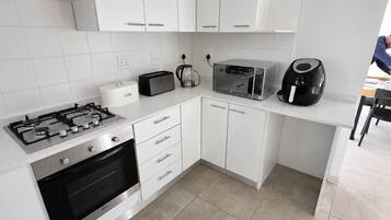 Una cocina moderna con armarios blancos, estufa a gas, horno, microondas y cafetera.