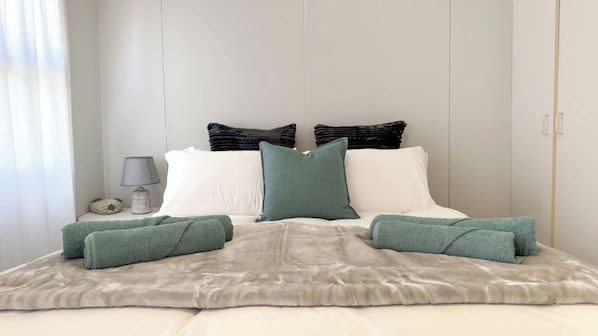 A bed with a grey blanket, two pillows, and a bedside lamp.