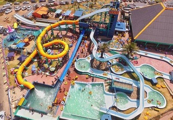 A water park with multiple slides and pools, surrounded by a parking area and buildings.