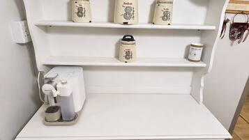 A kitchenette with a coffee machine, three storage containers, and a small shelf.